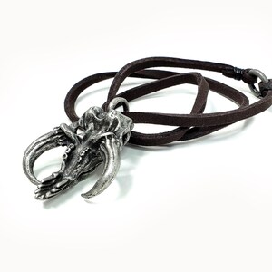 May include: A silver pendant shaped like a claw with a brown leather cord. The pendant has a detailed design and is a unique piece of jewelry.