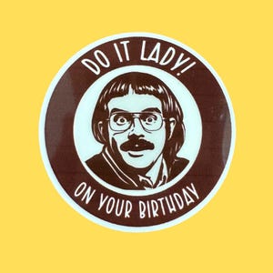 Op de afbeelding: Een ronde, bruin en witte afbeelding met een cartoon illustratie van een man met een snor en bril. De tekst "DO IT LADY! ON YOUR BIRTHDAY" staat rond het gezicht van de man.