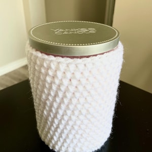 May include: White crocheted candle cozy with a silver lid that says "Yankee Candle" on top.