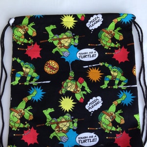 May include: Black drawstring bag with a Teenage Mutant Ninja Turtles print. The bag features images of the turtles, pizza slices, and the text "Tough as a Turtle!" and "...Pizza, Please!"