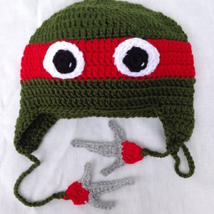 May include: Green and red crocheted hat with white eyes and two gray crocheted ninja stars.