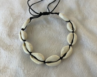 May include: A white seashell bracelet with black string. The bracelet is tied with a knot and has a simple design.