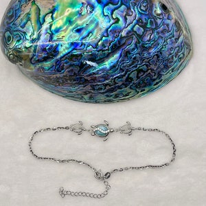 May include: A silver anklet with a blue abalone shell turtle charm. The anklet has a lobster clasp closure and an extension chain.