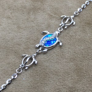 May include: Silver chain bracelet with three turtle charms. The center turtle charm features a blue opal stone with clear crystal accents.
