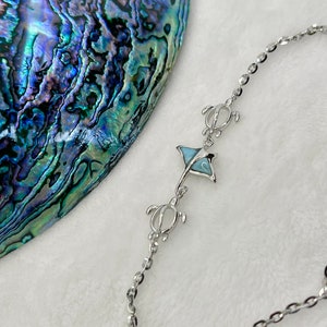 May include: A silver chain bracelet with a blue and white stingray charm and two turtle charms. The bracelet is on a white background.