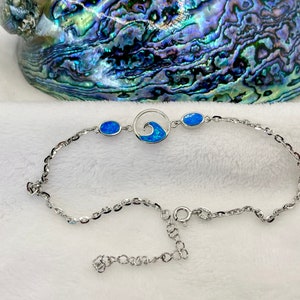 May include: A silver chain bracelet with a blue opal wave charm and two smaller blue opal stones. The bracelet has a lobster clasp closure.