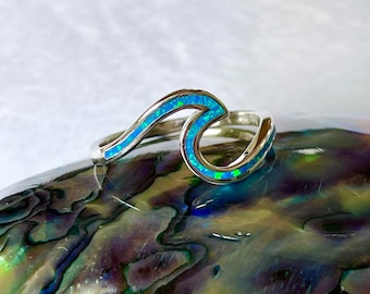May include: A silver wave ring with blue opal inlay. The ring is set on a iridescent abalone shell.