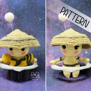 May include: A crocheted amigurumi doll wearing a yellow and black outfit and a brown hat. The doll is sitting on a white crocheted ring, resembling a planet. The background is a galaxy with stars.