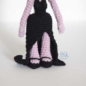 May include: Crocheted doll in a black dress with a split skirt, lavender arms and feet. The doll has a black headpiece and is wearing black shoes. The doll is handmade. The text "CHRISETTE DESIGNS" is visible.