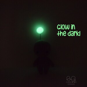 May include: A small, green, glow-in-the-dark plush toy with a round head and a small, green, glow-in-the-dark ball on top. The text "glow in the dark!" is written in green below the toy.