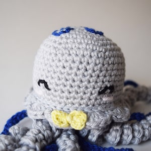 May include: A crocheted gray octopus with blue tentacles and a yellow bow tie. The octopus has a cute face with black eyes and a pink blush.