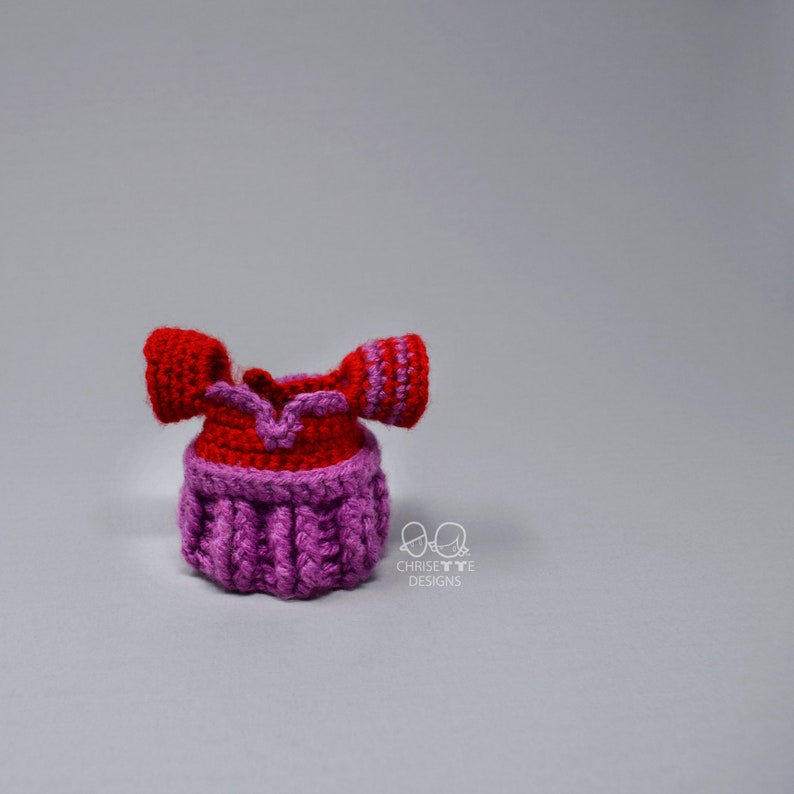 May include: A crocheted doll dress with red and pink yarn. The dress has a sweetheart neckline and short sleeves.