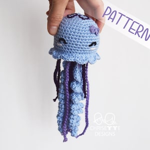 crochet yarn jellyfish doll with embroidered dark purple detail on top of it's head. Body is light blue with light and dark purple tentacles.