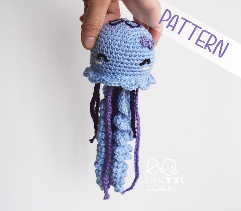 crochet yarn jellyfish doll with embroidered dark purple detail on top of it's head. Body is light blue with light and dark purple tentacles.