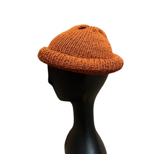 Może przedstawiać: Czapka beanie w kolorze wypalanej pomarańczy z zaokrąglonym wierzchołkiem i szerokim rondem.