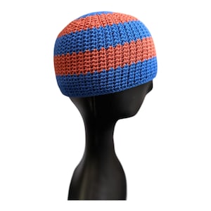 May include: A crocheted beanie hat with alternating horizontal stripes of blue and orange. The hat is displayed on a black mannequin head against a white background. The hat's texture is visible, showcasing the handmade quality.