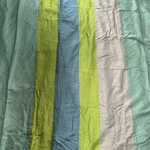 May include: A set of colorful, striped curtains. The vertical stripes alternate between shades of green, blue, and a pale gray. The fabric has a slightly wrinkled texture, and the curtains are hanging from clips.