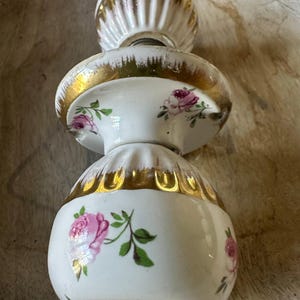 May include: A white and gold decorative object with a stacked design. The object features pink rose floral patterns and gold trim. The top and bottom sections have a ribbed design.