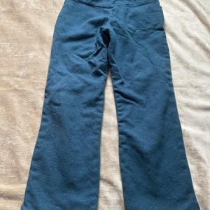 May include: Teal-colored pants with a drawstring waist. The pants have a flared leg design and are made of a soft, textured fabric. The pants are laid flat on a neutral-toned surface.