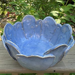May include: A large, handcrafted blue ceramic bowl with a unique, scalloped edge design. The bowl features embossed seashell patterns around the rim and a glossy finish. The bowl is a decorative piece for the home.