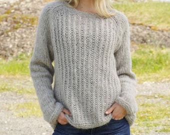 May include: A gray knitted sweater with a ribbed texture. The sweater has a round neckline and long sleeves. The model is wearing the sweater with blue jeans. DROPS DESIGN. www.garnstudio.com