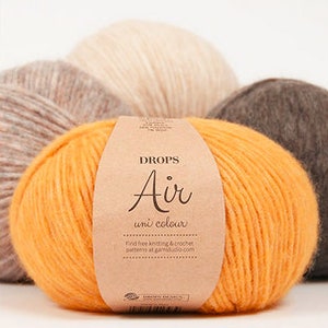 Puede incluir: Un ovillo de lana naranja con una etiqueta de papel marr&oacute;n. La etiqueta dice "DROPS Air uni colour" y "Find free knitting & crochet patterns at garnstudio.com".