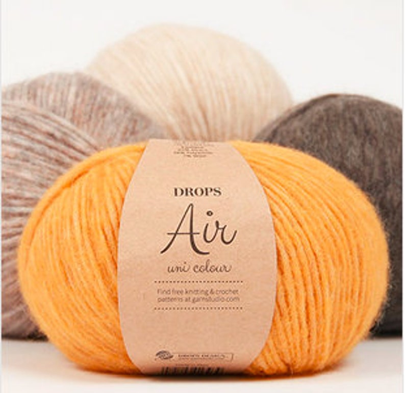 Puede incluir: Un ovillo de lana naranja con una etiqueta de papel marr&oacute;n. La etiqueta dice "DROPS Air uni colour" y "Find free knitting & crochet patterns at garnstudio.com".