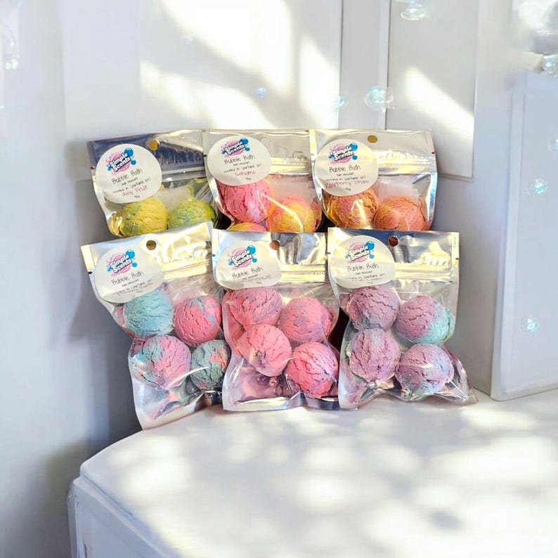 May include: Several clear plastic bags filled with colorful bath bombs. Each bag contains multiple spherical bath bombs in shades of pink, blue, yellow, and orange. The bags have labels with the text "Bubble Bath".