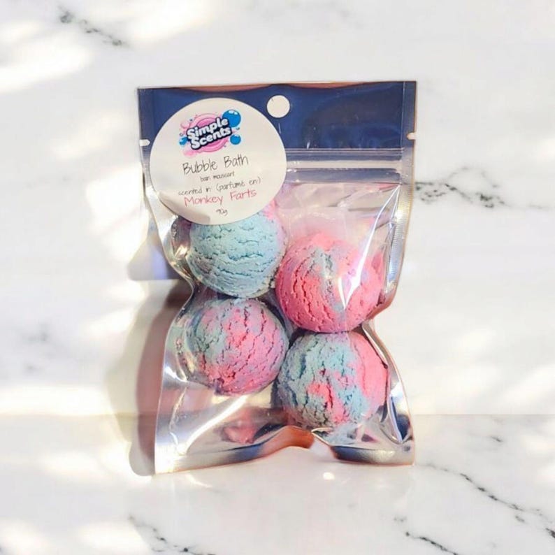 May include: A clear plastic bag containing four bubble bath bombs. The bath bombs are a mix of pink and blue colors. The bag has a white label with the text "Simple Scents Bubble Bath" and "Monkey Farts".