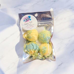 May include: A clear plastic bag containing four bubble bath bombs. The bath bombs are spherical, with a yellow and blue color scheme. The bag has a label that reads "Simple Scents" and "Bubble Bath" with "Juicy Fruit" text.