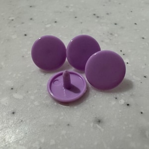 Può includere: Quattro bottoni a pressione color lavanda. Tre sono rotondi con una superficie liscia e uno ha un perno e una base circolare. Le chiusure sono in plastica e sono progettate per abbigliamento o artigianato.
