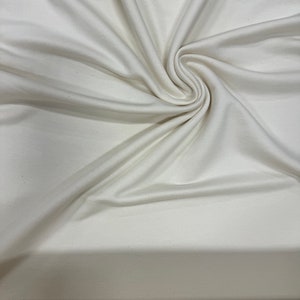 May include: Close-up of a white fabric with a smooth texture. The fabric is folded and draped, creating soft folds and curves.