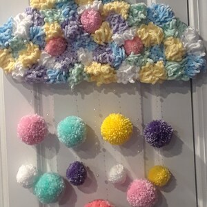 May include: A colorful yarn cloud with a string of pom-poms hanging from it. The pom-poms are in various colors, including pink, yellow, white, purple, and green.