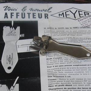 Puede incluir: Anuncio vintage de un afilador de cuchillos Meyer. El anuncio impreso en blanco y negro presenta diagramas y texto en francés, junto con un afilador de metal. El anuncio está en un papel doblado.
