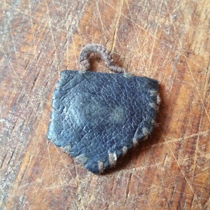Peut inclure: Une petite étiquette en cuir bleu foncé avec une boucle en cuir marron sur le dessus. L'étiquette est cousue sur les bords et a un aspect usé et vintage.