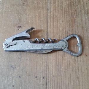 May include: Silver-toned metal bottle opener with a corkscrew and a bottle opener. The opener has the words "COGNAC Bisquit" engraved on it.