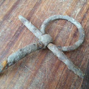 May include: A rusty metal ring with a knot in the centre. The ring is made of thick, twisted metal and has a rough, weathered surface.