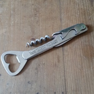 Peut inclure: Ouvre-bouteille et tire-bouchon argenté avec un ouvre-bouteille intégré. L'outil est gravé avec "Veuve Clicquot-Ponsardin".