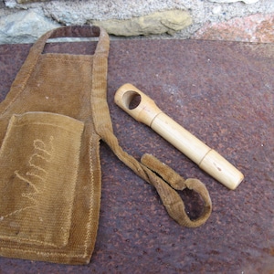 Può includere: Un grembiule di velluto a coste marrone con una tasca su cui è scritto "Mama". Un  schiaccianoci di legno è appoggiato sulla superficie arrugginita accanto al grembiule.