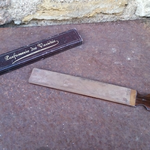 May include: A brown cardboard box with gold lettering that reads "Parfumerie Des Varietes" and a wooden straight razor with a brown wooden handle.