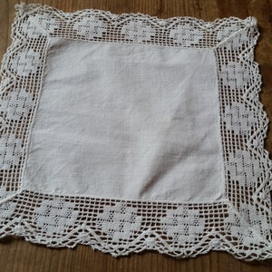 May include: White square linen doily with a delicate crocheted lace border.