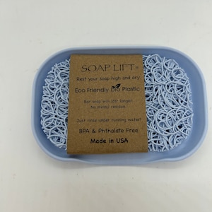 May include: A light blue soap dish made of eco-friendly bio plastic. The dish is designed to keep soap elevated and dry, preventing it from becoming soggy. The text on the label reads "SOAP LIFT, Rest your soap high and dry, Eco Friendly bio Plastic, Bar soap will last longer. No messy residue. Just rinse under running water! BPA & Phthalate Free, Made in USA."
