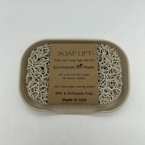 May include: A beige soap dish made of eco-friendly bio plastic with a white soap lift inside. The soap lift is made of a woven material and is designed to keep soap bars elevated and dry. The dish has the text "SOAP LIFT&reg;" and "Rest your soap high and dry" on the front. The dish also has the text "Eco Friendly Bio Plastic", "Bar soap will last longer. No messy residue." and "Just rinse under running water! BPA & Phthalate Free Made in USA" on the front.