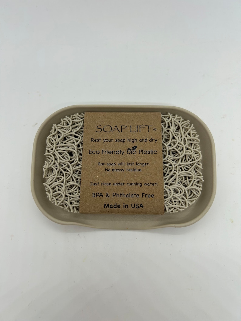 May include: A beige soap dish made of eco-friendly bio plastic with a white soap lift inside. The soap lift is made of a woven material and is designed to keep soap bars elevated and dry. The dish has the text "SOAP LIFT&reg;" and "Rest your soap high and dry" on the front. The dish also has the text "Eco Friendly Bio Plastic", "Bar soap will last longer. No messy residue." and "Just rinse under running water! BPA & Phthalate Free Made in USA" on the front.