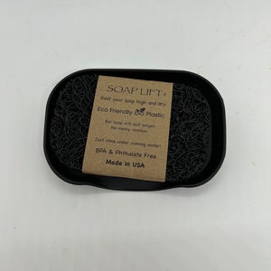 May include: Black soap dish made of eco-friendly bio plastic. The dish has a raised center to keep soap elevated and dry. The label reads "SOAP LIFT", "Rest your soap high and dry", "Eco Friendly bio Plastic", "Bar soap will last longer. No messy residue.", "Just rinse under running water!", "BPA & Phthalate Free", "Made in USA".