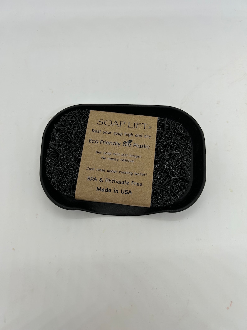 May include: Black soap dish made of eco-friendly bio plastic. The dish has a raised center to keep soap elevated and dry. The label reads "SOAP LIFT", "Rest your soap high and dry", "Eco Friendly bio Plastic", "Bar soap will last longer. No messy residue.", "Just rinse under running water!", "BPA & Phthalate Free", "Made in USA".