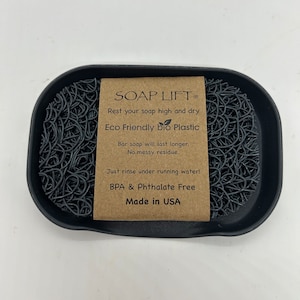 May include: A black soap dish made of eco-friendly bio plastic. The dish is designed to keep soap elevated and dry, preventing it from becoming soggy. The dish is BPA and Phthalate free and made in the USA. The text on the label reads "SOAP LIFT&reg; Rest your soap high and dry Eco Friendly bio Plastic Bar soap will last longer. No messy residue. Just rinse under running water! BPA & Phthalate Free Made in USA"