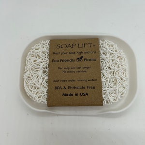 May include: White soap dish made of eco-friendly bio plastic. The dish is designed to keep soap elevated and dry, preventing messy residue. The dish is BPA and Phthalate free and made in the USA. The text on the label reads "SOAP LIFT, Rest your soap high and dry, Eco Friendly bio Plastic, Bar soap will last longer. No messy residue. Just rinse under running water! BPA & Phthalate Free, Made in USA."
