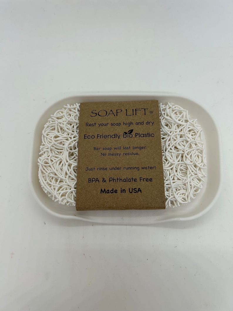 May include: White soap dish made of eco-friendly bio plastic. The dish is designed to keep soap elevated and dry, preventing messy residue. The dish is BPA and Phthalate free and made in the USA. The text on the label reads "SOAP LIFT, Rest your soap high and dry, Eco Friendly bio Plastic, Bar soap will last longer. No messy residue. Just rinse under running water! BPA & Phthalate Free, Made in USA."