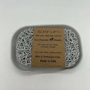 May include: White soap dish made of eco-friendly bio plastic. The dish is shaped like a web and has a label that reads "SOAP LIFT&reg; Rest your soap high and dry Eco Friendly bio Plastic Bar soap will last longer. No messy residue. Just rinse under running water! BPA & Phthalate Free Made in USA"